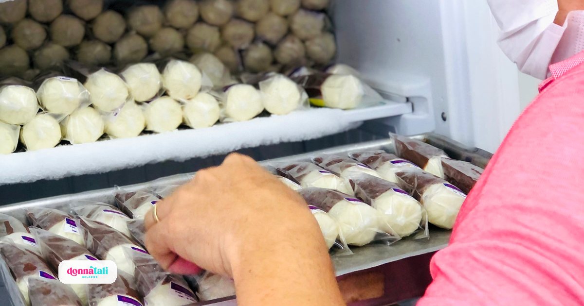 Talita organizando bandejas de geladinhos Donnatali embalados dentro de um freezer cheio de estoque