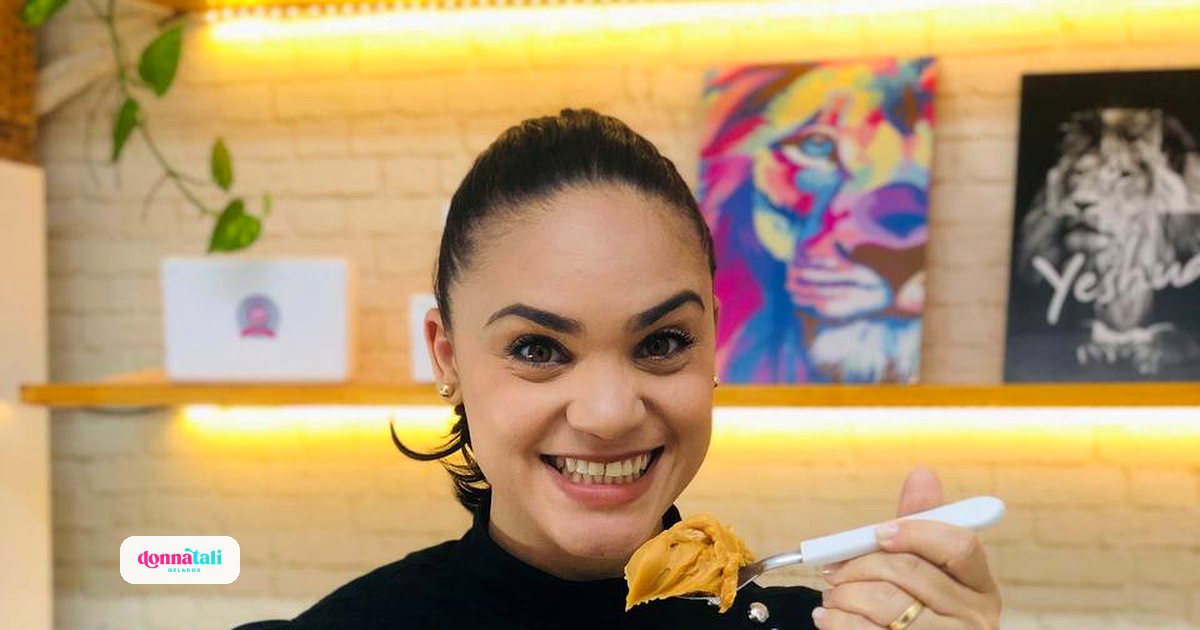 Talita, da Donnatali Gelados, sorrindo na sua loja com um pote de geladinho gourmet na mão
